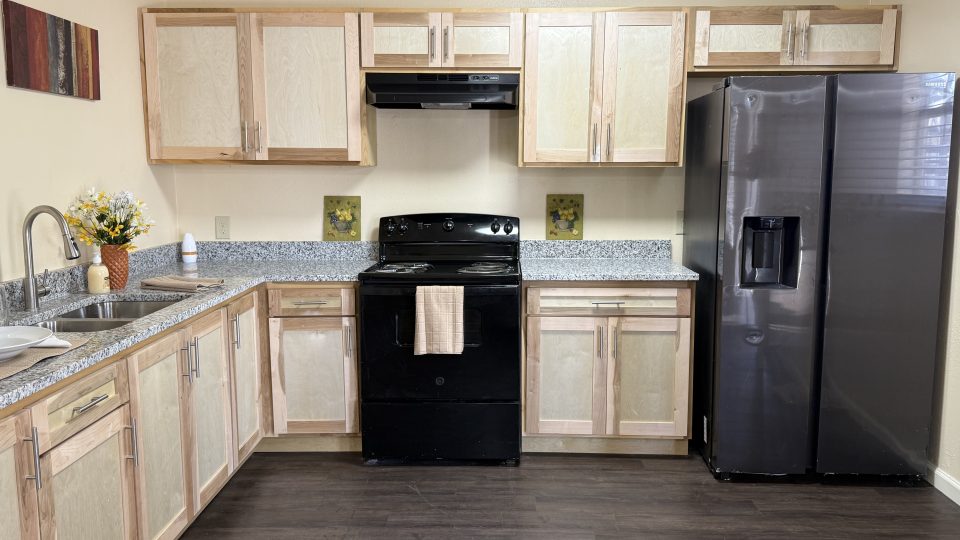 a kitchen with black appliances and wood cabinets at The Delmar Place Apartment